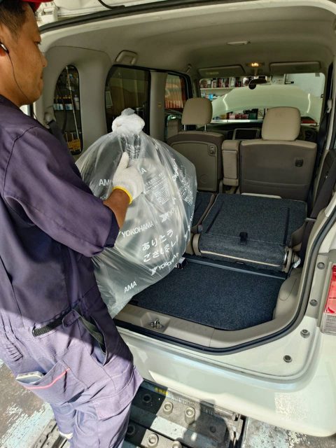 袋に入れた夏タイヤを車の荷室に積み込むスタッフ